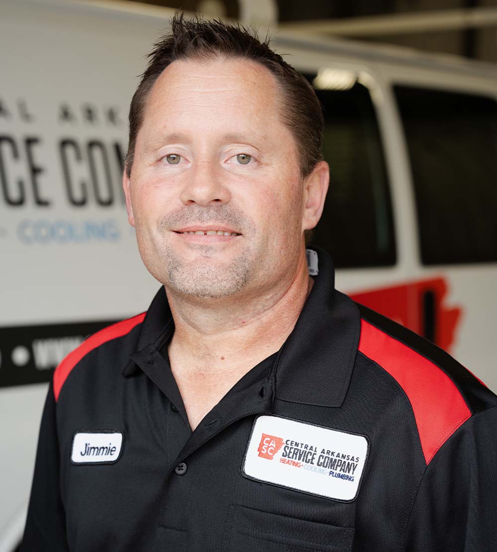 A man in a black and red company shirt stands in front of a van, exuding a relaxed and approachable vibe.